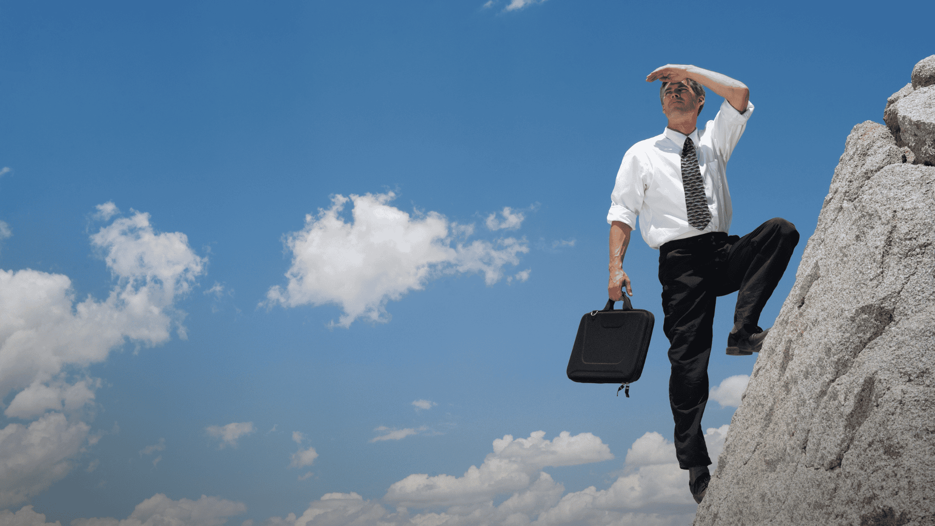 Businessman climbing a steep rock face, symbolizing the challenge of being out of work and stuck in a difficult job search.