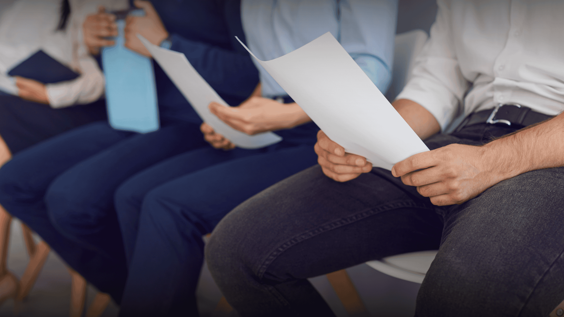 Candidates sitting in a row holding resumes in a waiting room, symbolizing why job seekers often undervalue their professional experience.